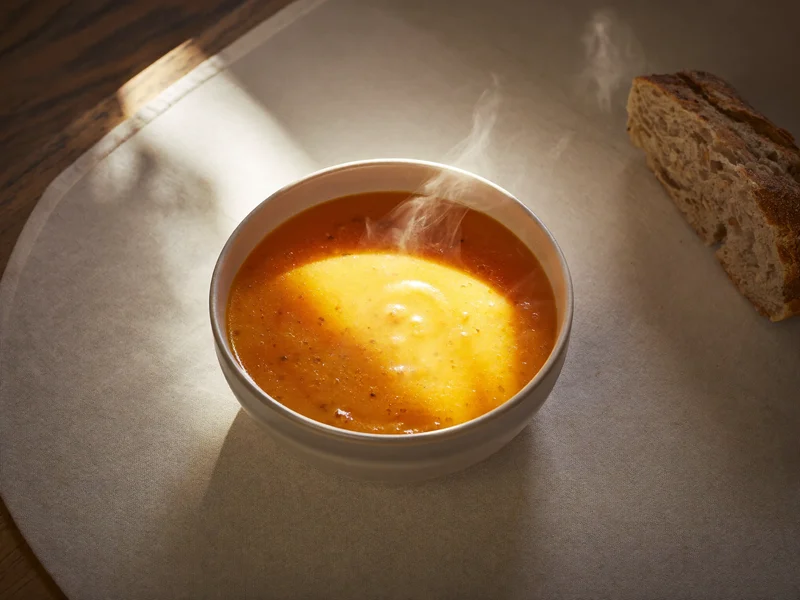 Illustration: steaming orange vegetable soup with a wholemeal roll on a linen placemat